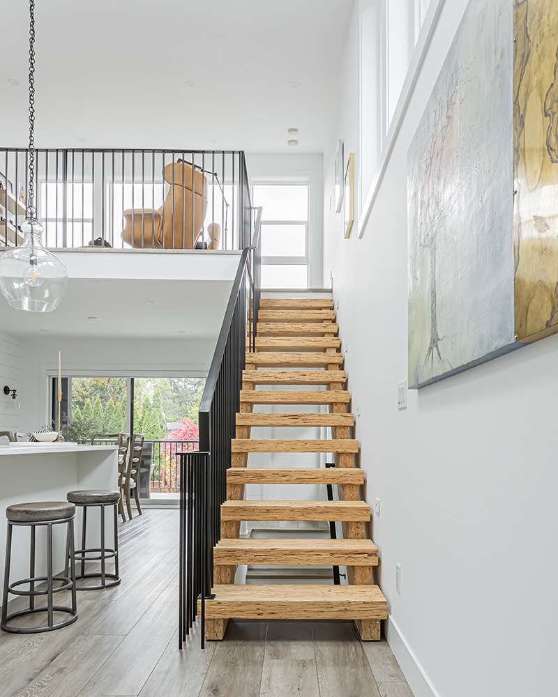 A wooden staircase with a black railing, with natural light, highlights the meticulous work of home renovation contractors in Langley, BC