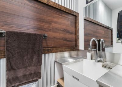 A custom additions modern bathroom with a white sink, a brown towel hanging on a rack, and a wooden panel behind it by Bowline Construction in Langley, BC