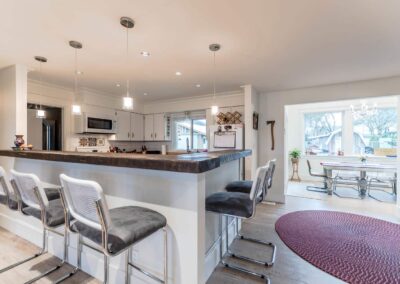A kitchen counter with a dark wood top and gray bar stools, leading into a dining area with a white table and chairs.