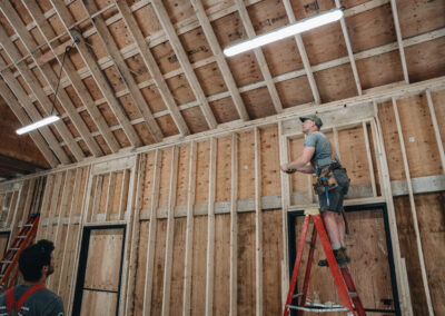 Bowline Construction team member on a ladder holding a measuring tape for pole barn construction in Langley, BC