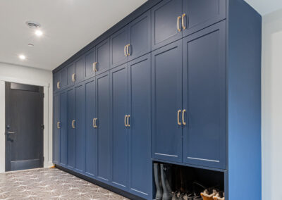 A spacious mudroom or hallway featuring a long wall of dark blue built-in cabinets with gold handles.
