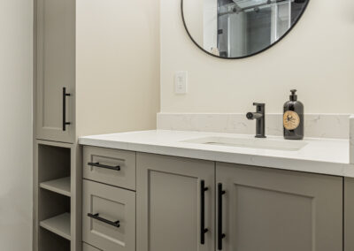 A bathroom with a glass shower enclosure, a dark vanity cabinet, a round mirror, and a wall with striped panels.