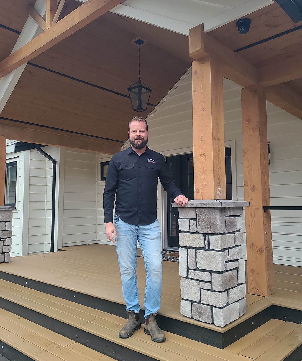 Reuben of Bowline Construction standing on a recently renovated home with wooden pillars and white siding in Langley, BC