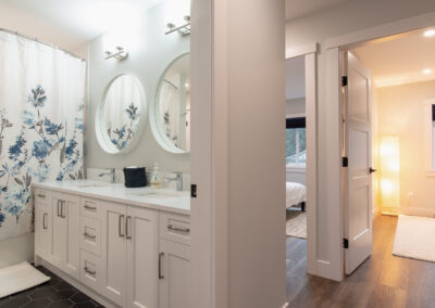 A bathroom with a double vanity, two round mirrors, a floral shower curtain, and an open doorway leading to another room.