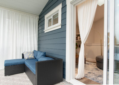 A patio featuring a dark rattan wicker sectional sofa with blue cushions, similar to a Walsunny 3-piece set, with white curtains and a sliding glass door leading indoors.