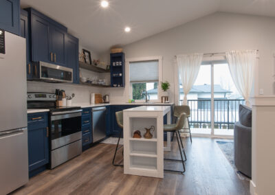 A modern kitchen with dark blue cabinets, stainless steel appliances, a small white island, and sliding glass doors leading to a balcony.
