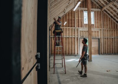 Bowline Construction team members on a ladder holding a measuring tape for pole barn construction in Langley, BC