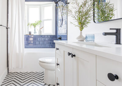 A modern bathroom with dark blue subway tile, a white vanity with a quartz countertop, black hardware, and a chevron patterned floor.
