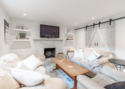 A bright living room with white shiplap walls, a painted brick fireplace, a mounted TV, and a sliding barn door with black hardware custom additions in Langley, BC