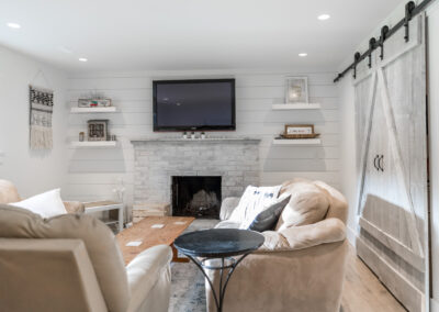 a living room featuring white walls, a stone fireplace, floating shelves, a mounted flat-screen TV, and a rustic sliding barn door