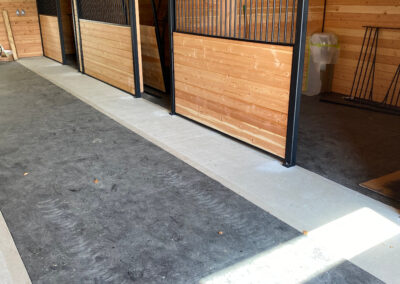 A long, well-lit barn aisle with horse stalls on either side by pole barn construction contractors in Langley, BC