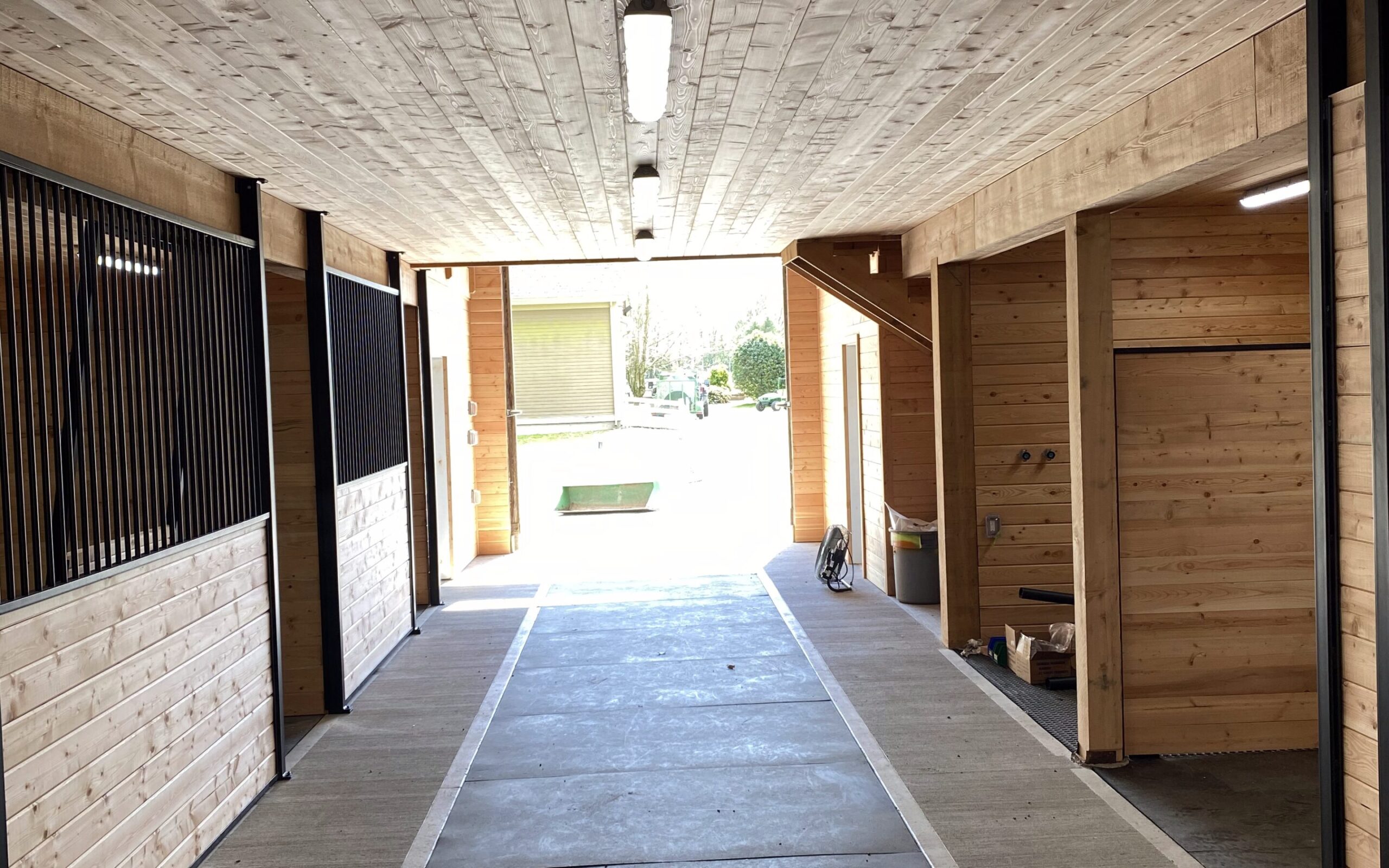 A long, well-lit barn aisle with horse stalls on either side by pole barn construction contractors in Langley, BC