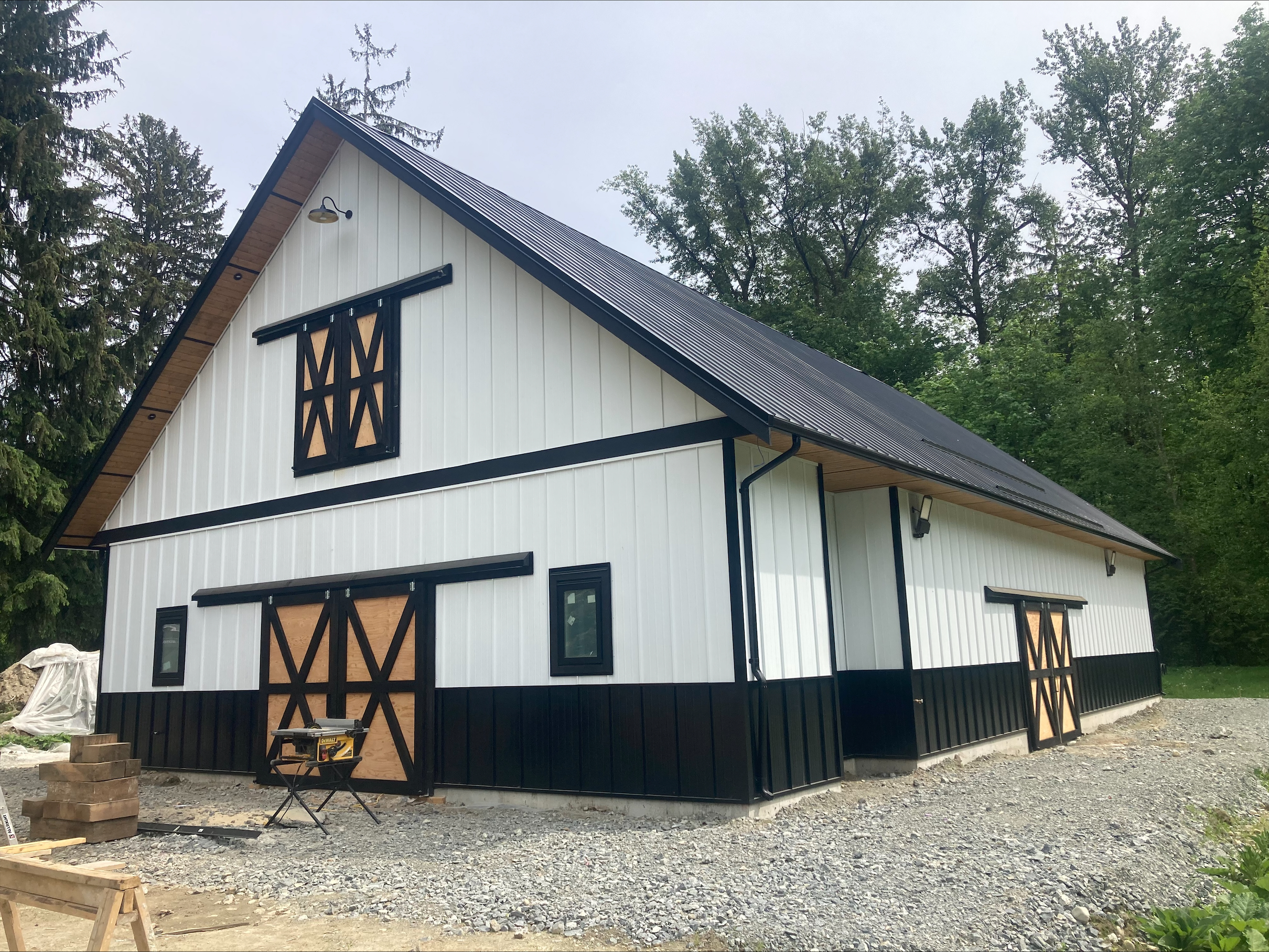 A black roof pole barn with white siding and several doors in in Langley