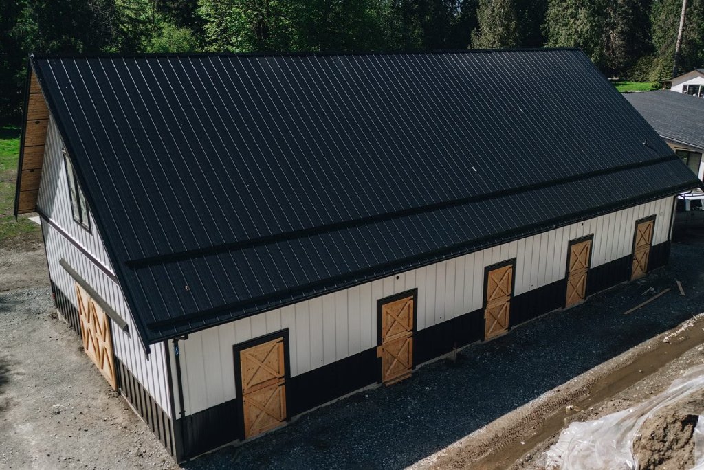 A black roof with white siding and several doors in a process of pole barn construction in Langley