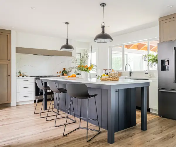 Modern custom homes kitchen with large charcoal island, three black bar stools, pendant lights, marble-look backsplash, and wood floors by Bowline Construction in Langley, BC