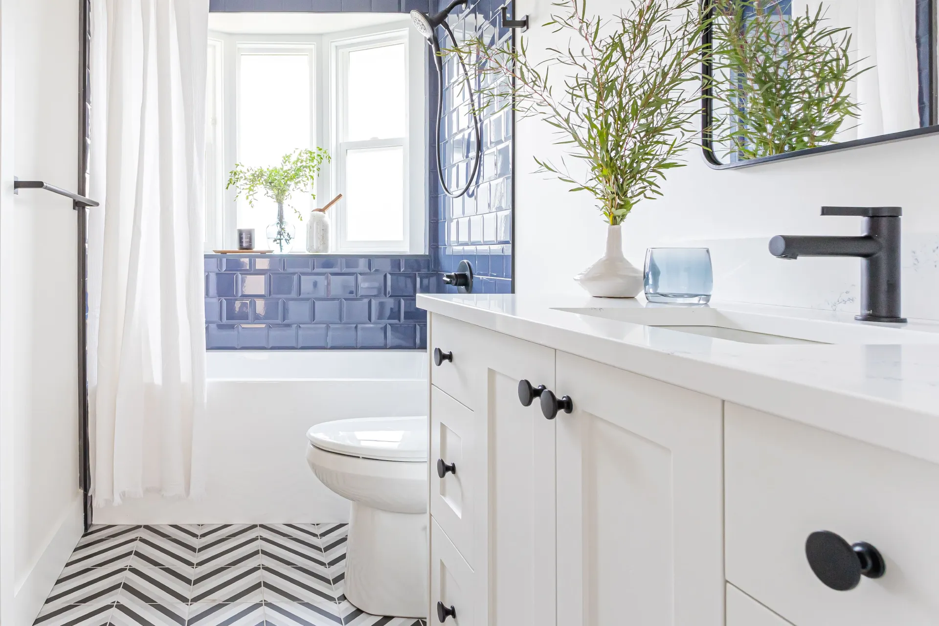 Home addition bathroom remodel with white vanity, black fixtures, blue subway tile tub surround, and herringbone tile floor by Bowline Construction