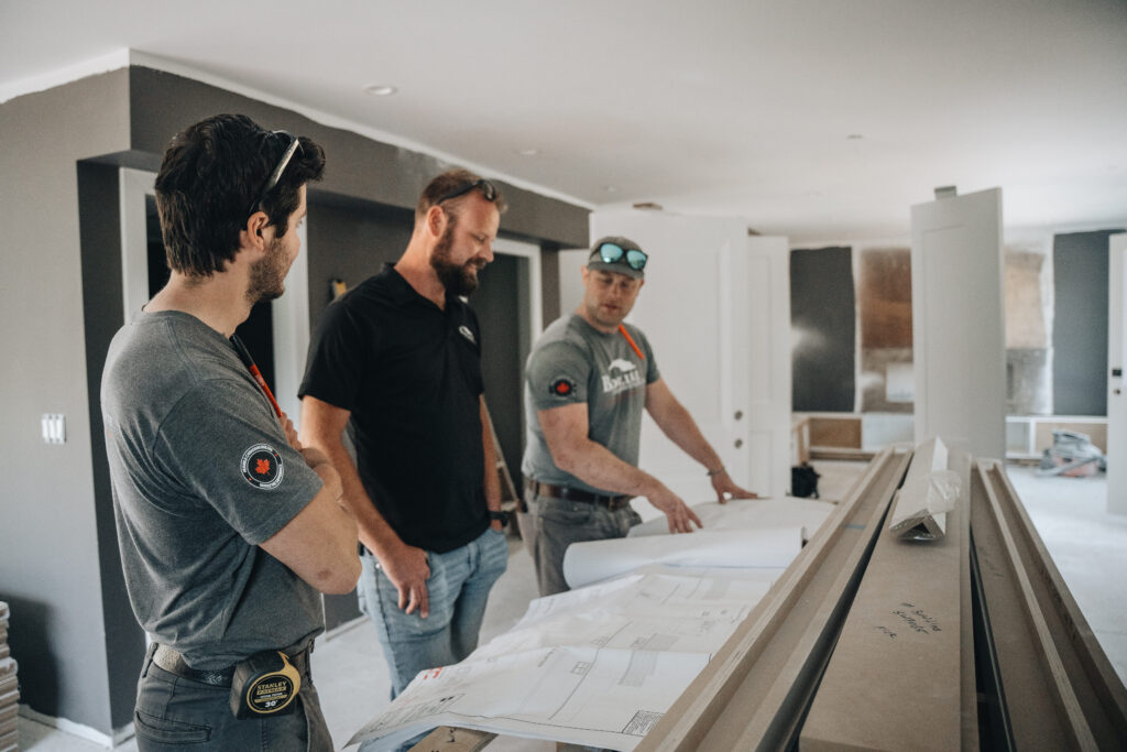 Three builders reviewing plans and interior framing for an in-law suite versus legal suite project in Langley City by Bowline Construction.