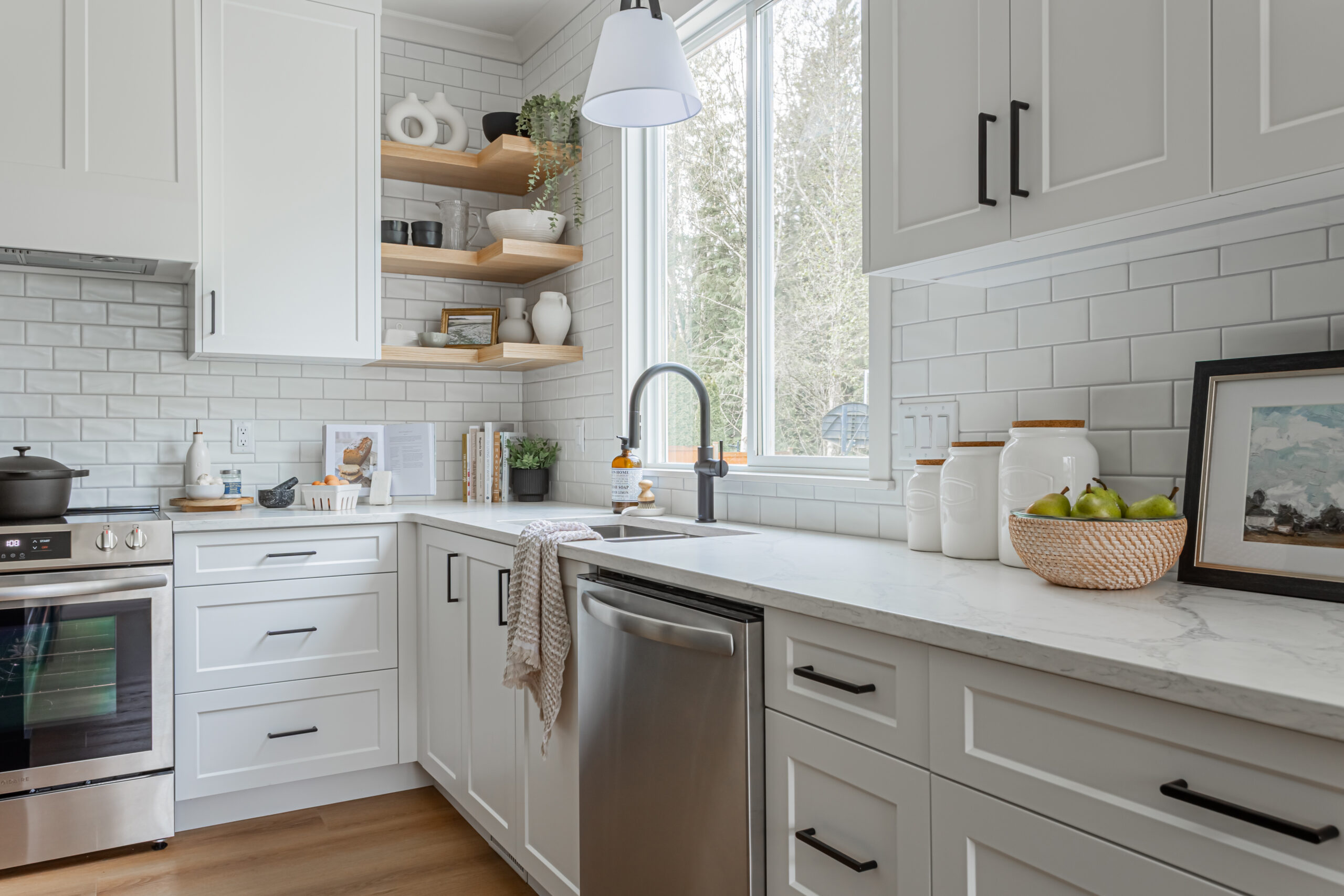 Bright white shaker-style kitchen cabinets with black matte handles, subway tile backsplash, quartz countertops, and floating corner shelves, completed by a kitchen contractor and kitchen renovation company in Langley City by Bowline Construction.